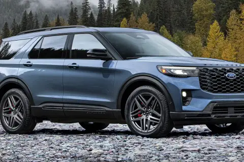 Niebieski Ford Explorer Sport ST na kamienistej plaży, z jesiennym lasem w tle.