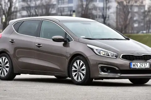 Brązowy Kia Ceed JD na tle budynków i drzew. Elegancki, miejski samochód gotowy na każdą podróż.