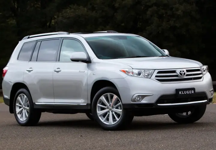Srebrny Toyota Kluger zaparkowany na drodze, z ciemnym tłem drzew.
