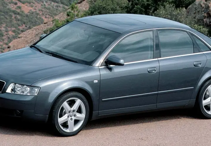 Szary sedan Audi A4 B6, produkowany w latach 2000-2006, parkuje na tle górskiego krajobrazu.