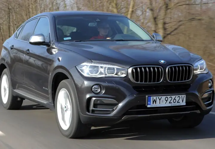 Ciemnoszary BMW F16 z kierowcą w czerwonej bluzie jedzie po drodze.