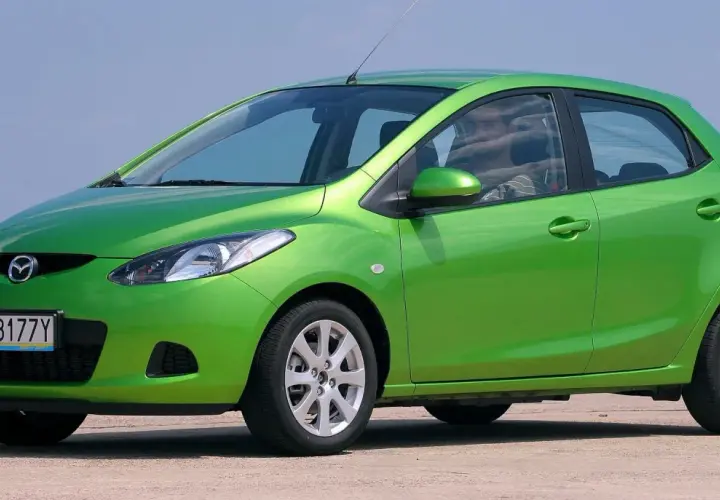 Zielona Mazda 2 DE z polskimi tablicami rejestracyjnymi WY 8177Y stoi na zewnątrz.