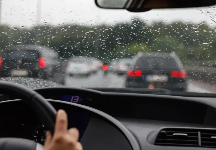 Widok z wnętrza samochodu na deszczową drogę z innymi autami i kroplami na szybie.
