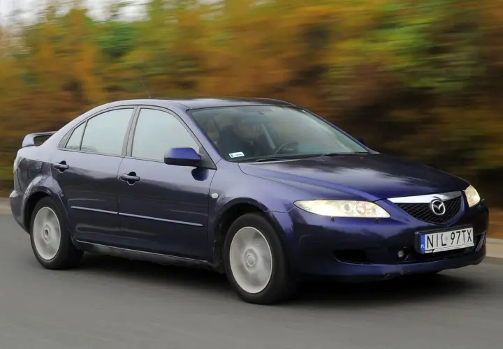 Granatowa Mazda 6 GG jedzie po drodze, za nią rozmyty krajobraz jesiennych drzew.