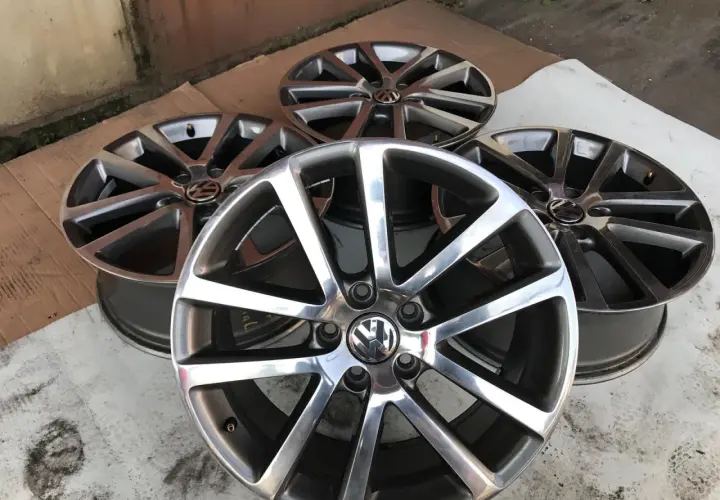 Cztery aluminiowe felgi Volkswagen z logo, ułożone na ziemi.