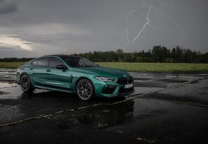 Zielony BMW M8 Competition Gran Coupé na mokrym asfalcie, z błyskawicą na burzowym niebie.