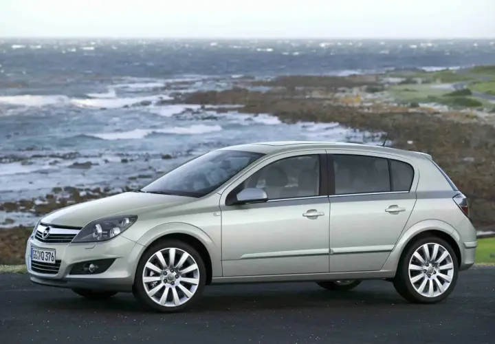 Srebrny Opel Astra H, popularny model z lat produkcji 2004-2009, zaparkowany na tle skalistego wybrzeża i wzburzonego morza.