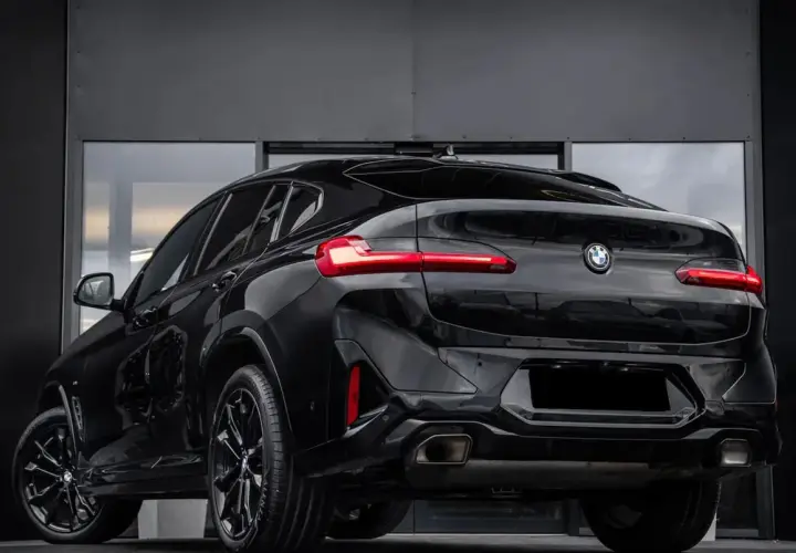Elegancki, czarny BMW X4 G02 z przyciemnianymi szybami i sportowymi felgami prezentuje się imponująco na tle nowoczesnej, szarej ściany.