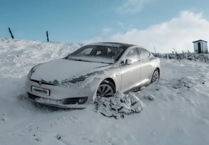 Srebrny samochód Tesla w śniegu, z widocznym logo marki.
