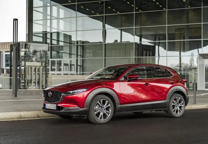 Czerwona Mazda CX-30 lśni przed nowoczesnym budynkiem z przeszkloną fasadą.