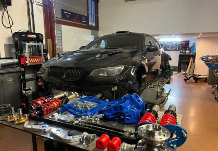 Warsztat z czarnym BMW E92, częściami zawieszenia i narzędziami. Lata produkcji tego modelu to 2006-2013.