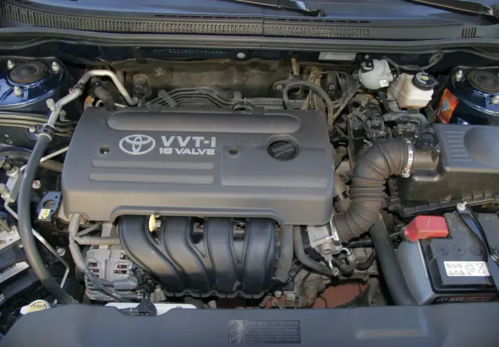 Silnik VVT-i 16 Valve z Toyoty Corolla E12. Widoczny alternator, akumulator i elementy układu dolotowego.