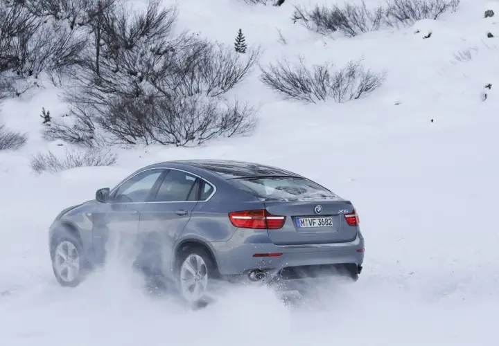 Szary BMW E71 X6 z napędem na cztery koła pokonuje zaspy śnieżne, unosząc chmury białego puchu.