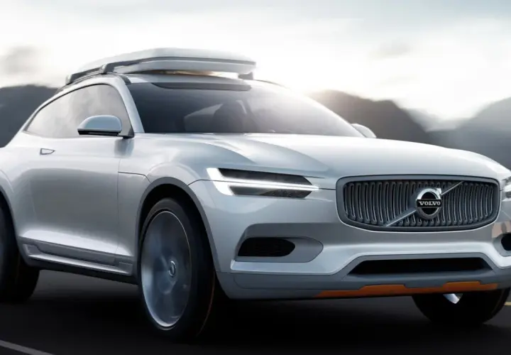 Biały Volvo XC100 z bagażnikiem dachowym jedzie po drodze, otoczony górami.