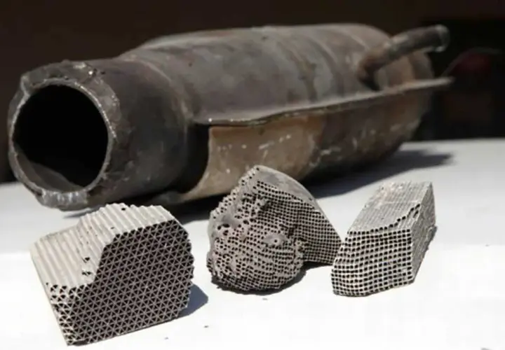 Rozcięty katalizator samochodowy z widocznym wkładem ceramicznym o strukturze plastra miodu.