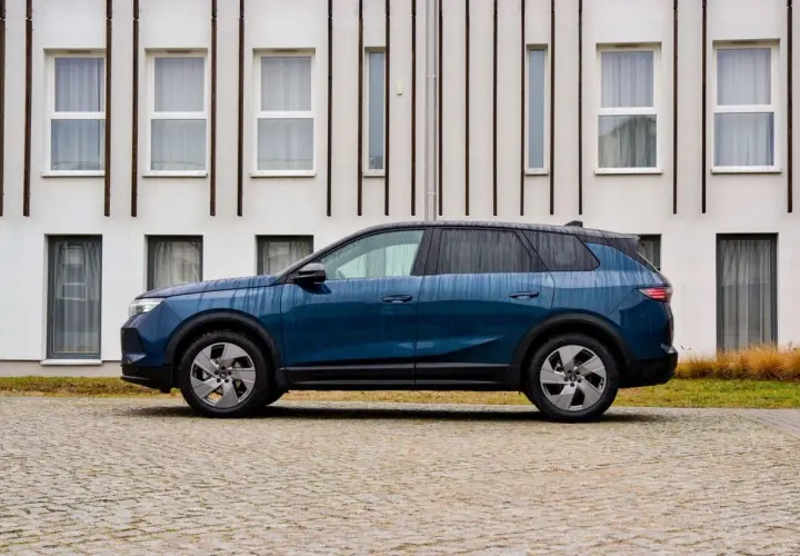 Nowoczesny, granatowy Opel hybryda stoi na brukowanym podjeździe przed minimalistycznym budynkiem.