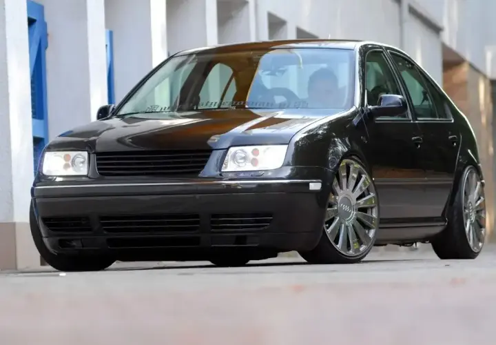 Czarny Volkswagen Bora z chromowanymi felgami stoi na ulicy.