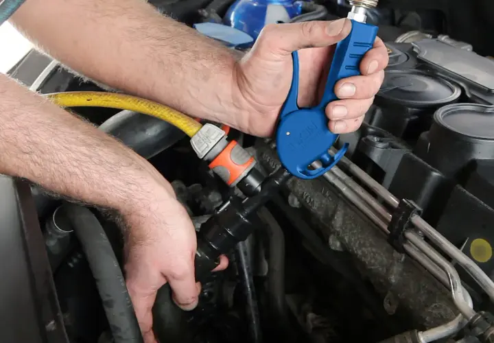 Ręce mechanika podłączają żółty wąż do niebieskiego narzędzia przy silniku samochodu.