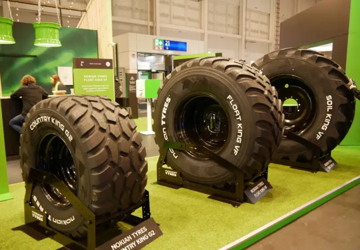 Trzy duże opony rolnicze Nokian Tyres na zielonej wykładzinie.