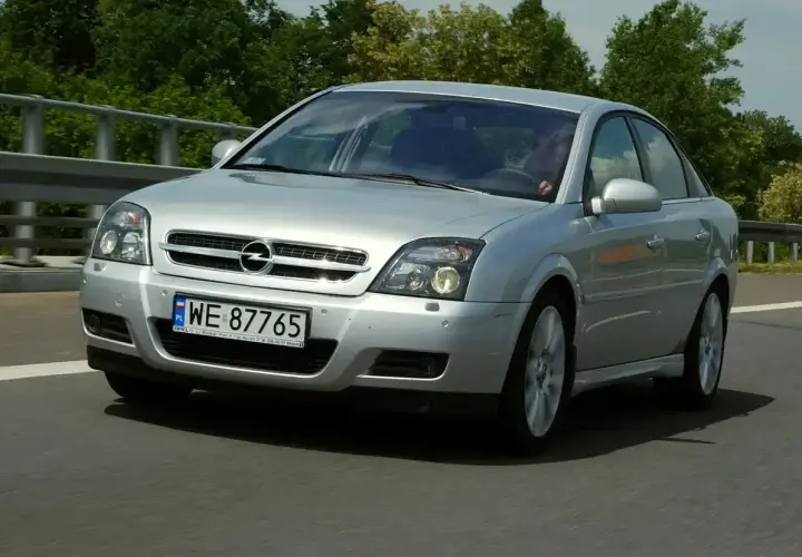 Srebrny Opel Vectra C GTS z polskimi tablicami WE 87765 jedzie po drodze, otoczony zielenią.