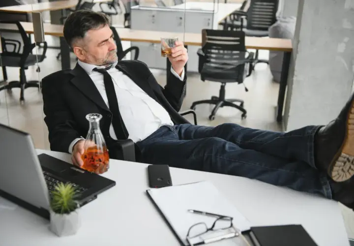 Mężczyzna w garniturze z alkoholem w ręku, zastanawia się, czy pracodawca może sprawdzać alkomatem.