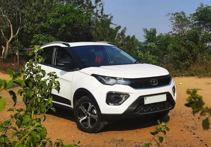 Biały Tata Nexon stoi na piaszczystej drodze, otoczony zielenią.