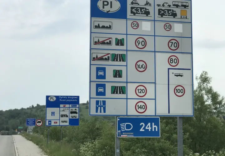 Znaki drogowe z limitami prędkości i informacją o opłatach drogowych na drodze ekspresowej.