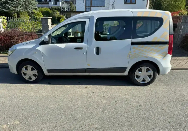 Biały Renault Dokker z żółtymi naklejkami na tylnej części, zaparkowany na ulicy.
