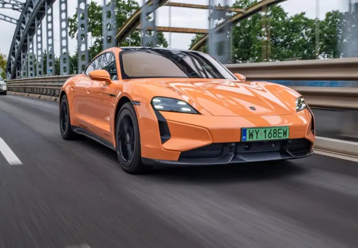 Pomarańczowy Porsche Taycan Turbo S pędzi po moście, jego sportowy design podkreślony przez dynamiczne linie.
