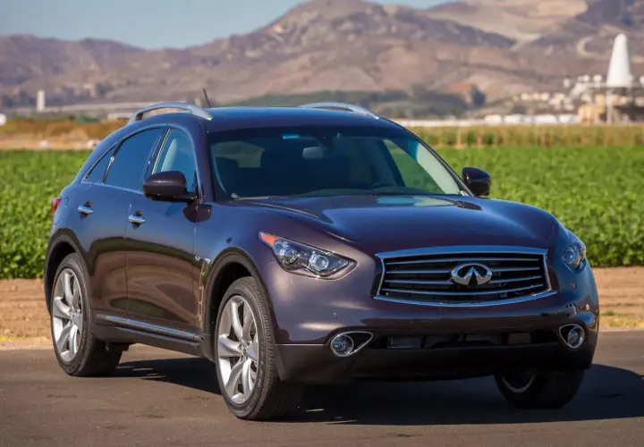 Elegancki, ciemnobordowy Infiniti QX70 stoi na tle krajobrazu z polami i górami.