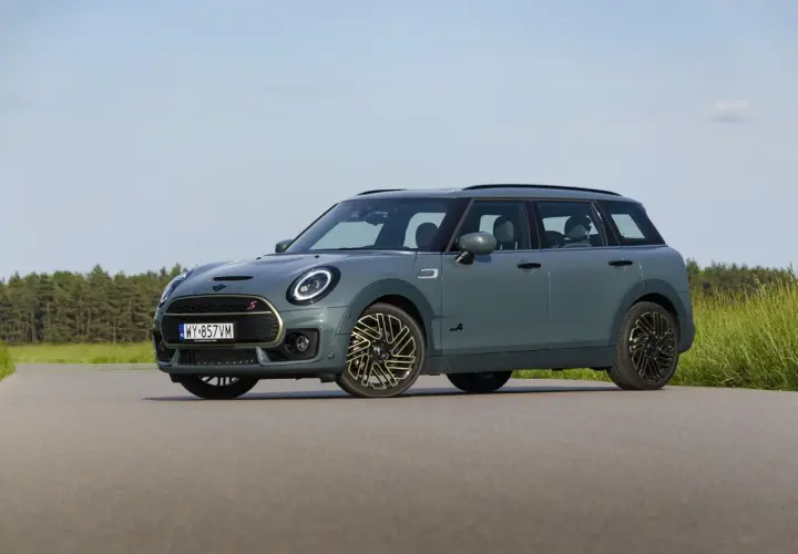 Szary Mini Clubman F54 z napędem ALL4 na tle lasu i łąki.