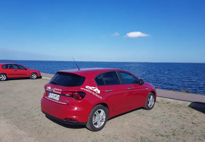Czerwony fiat tipo sedan zaparkowany nad błękitnym jeziorem.