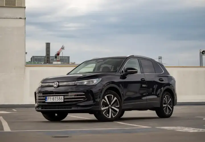 Czarny VW Tiguan Allspace na parkingu pod chmurką. Elegancki SUV z chromowanymi detalami i nowoczesnymi felgami.