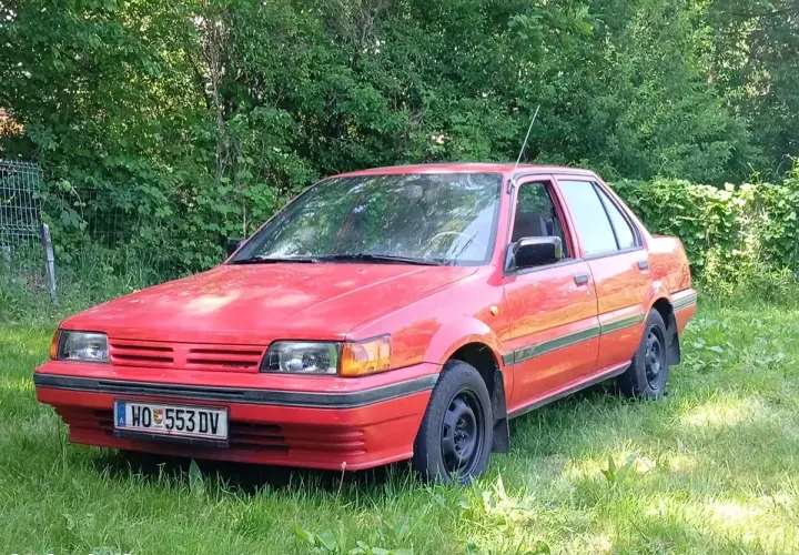Czerwony Nissan Sunny N13, klasyk z lat 80., stoi na trawie, gotowy na nowe przygody.