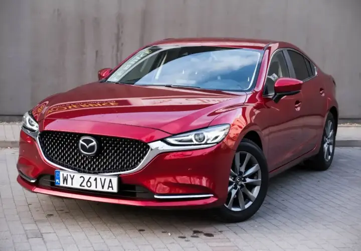 Czerwona Mazda 6 2.0 benzyna zaparkowana na kostce brukowej. Elegancka linia nadwozia i charakterystyczny grill.