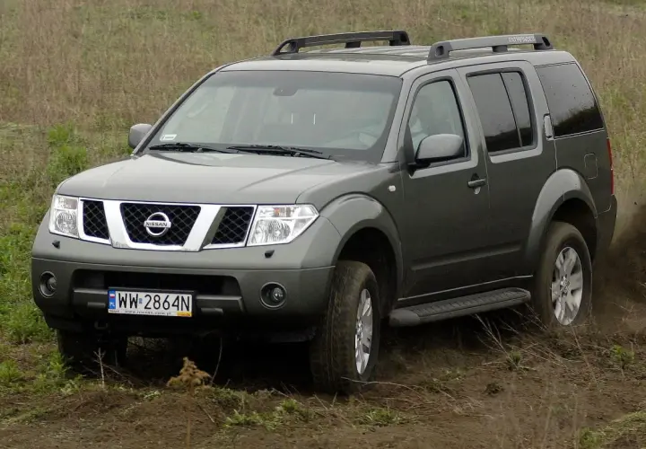 Szary Nissan Pathfinder r51 pokonuje błotniste wzniesienie, wzbijając tumany kurzu.