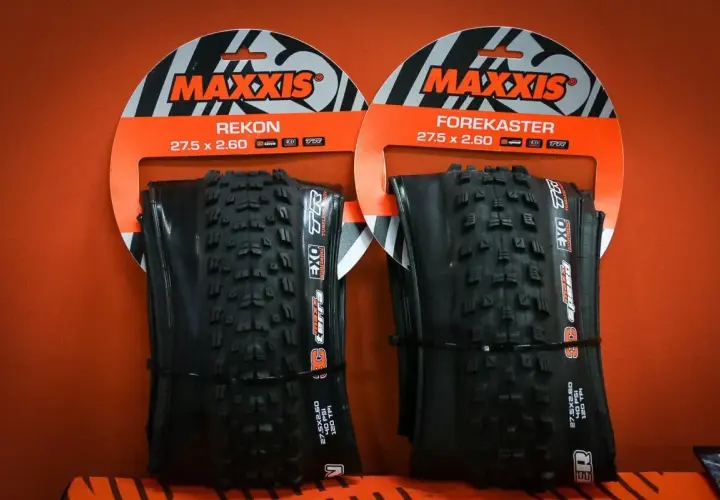 Dwie opony rowerowe Maxxis Rekon i Forekaster 27.5 x 2.60 na pomarańczowym tle.