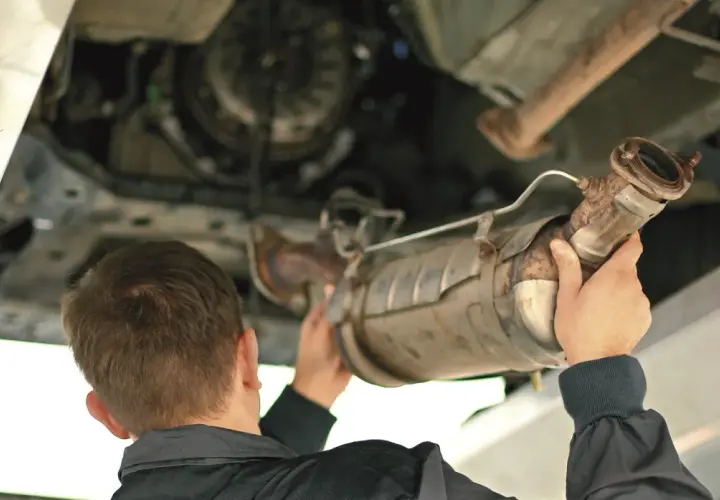 Mechanik trzymający pod samochodem zardzewiały element układu wydechowego, prawdopodobnie DPF.