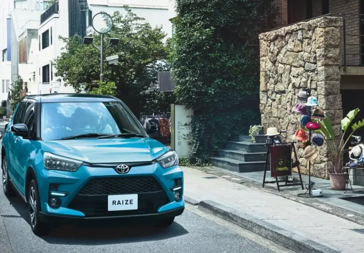 Turkusowy Toyota Raize parkuje na wąskiej uliczce z kamienną ścianą i wystawą kapeluszy.