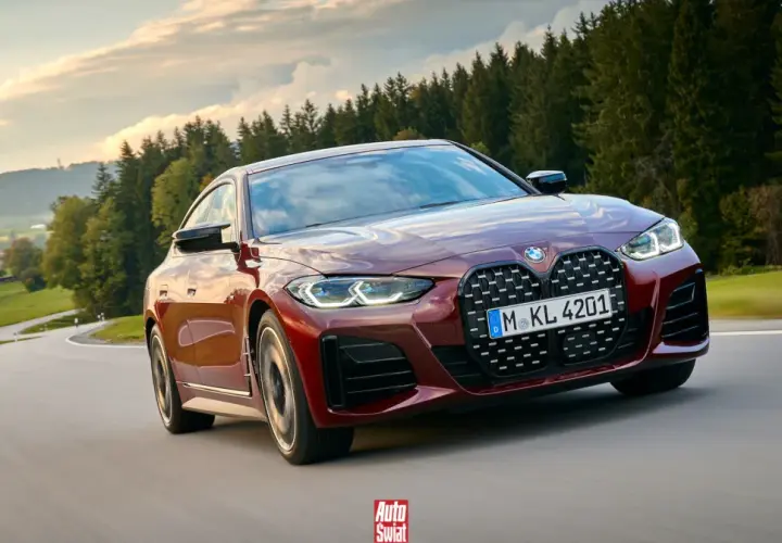 Czerwone BMW G26 z charakterystycznym grillem pędzi po krętej drodze wśród zielonych wzgórz i lasów.