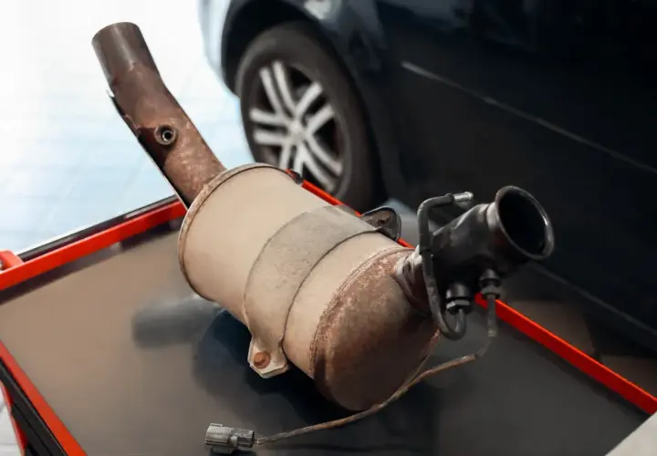 Filtr DPF na stole warsztatowym, z widocznym elementem wydechowym i złączem elektrycznym.