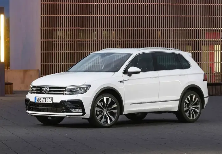 Biały Volkswagen Tiguan 5N z przyciemnianymi szybami i chromowanymi listwami, zaparkowany przed nowoczesnym budynkiem.