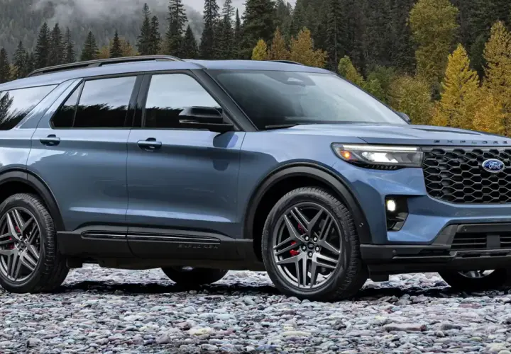 Niebieski Ford Explorer Sport ST na kamienistej plaży, z jesiennym lasem w tle.