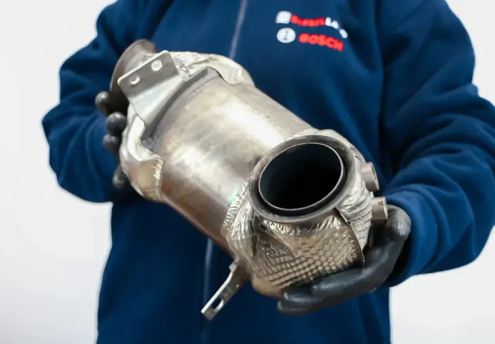 Mechanik w rękawiczkach trzyma katalizator, element układu wydechowego. Rozważasz wyprogramowanie DPF?
