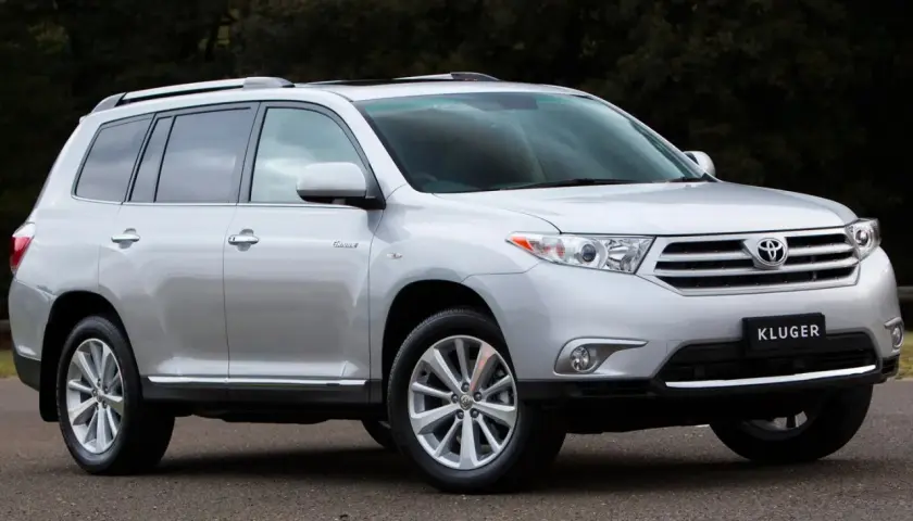 Srebrny Toyota Kluger zaparkowany na drodze, z ciemnym tłem drzew.