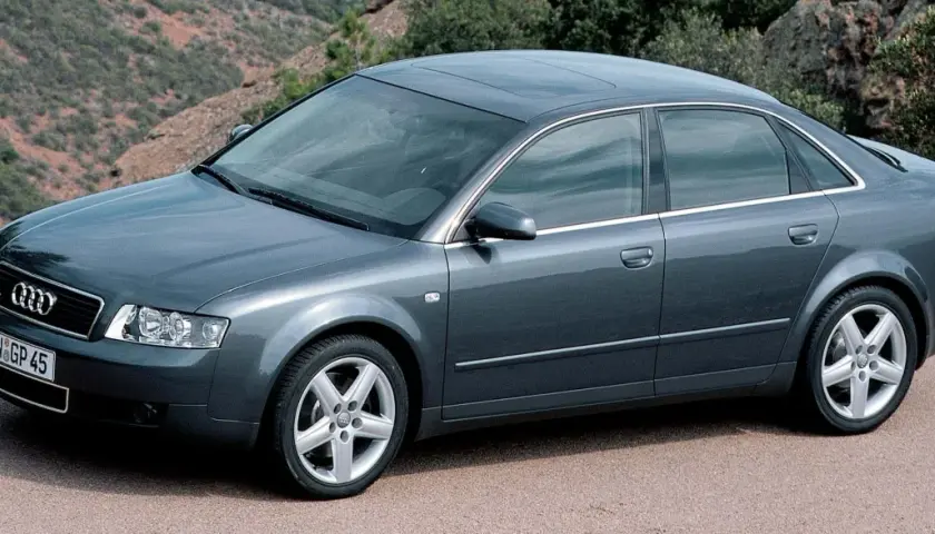 Szary sedan Audi A4 B6, produkowany w latach 2000-2006, parkuje na tle górskiego krajobrazu.