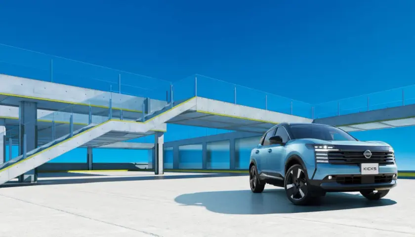Niebieski Nissan Kicks stoi na betonowym placu przed nowoczesnym budynkiem z przeszklonymi oknami i betonowymi schodami.