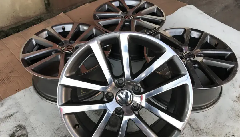 Cztery aluminiowe felgi Volkswagen z logo, ułożone na ziemi.