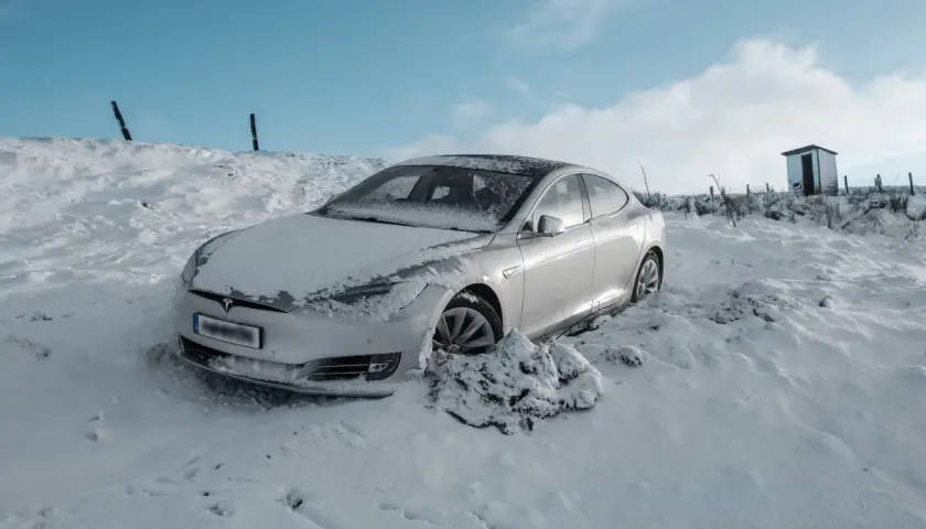 Srebrny samochód Tesla w śniegu, z widocznym logo marki.