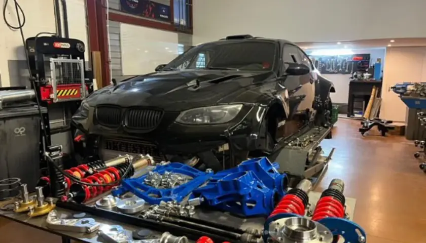 Warsztat z czarnym BMW E92, częściami zawieszenia i narzędziami. Lata produkcji tego modelu to 2006-2013.